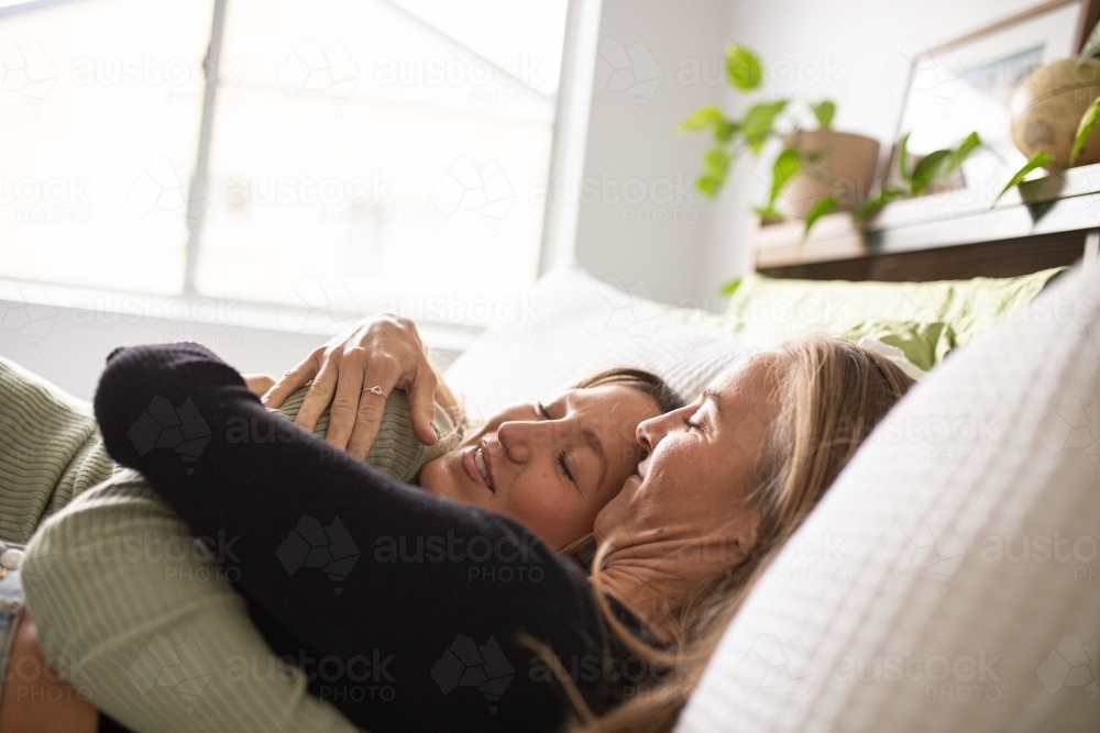 Two blonde women on the bed with white sheets cuddling and hugging eachother - Australian Stock Image
