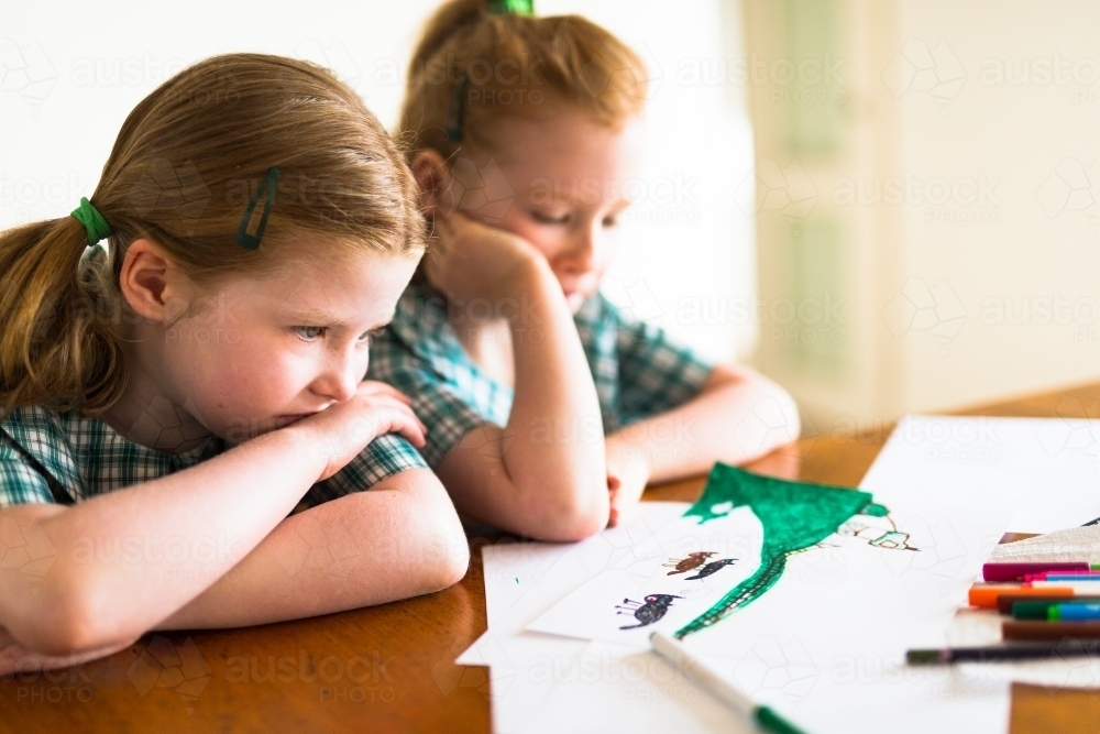 Two bored young school girls look at drawings at a desk - Australian Stock Image