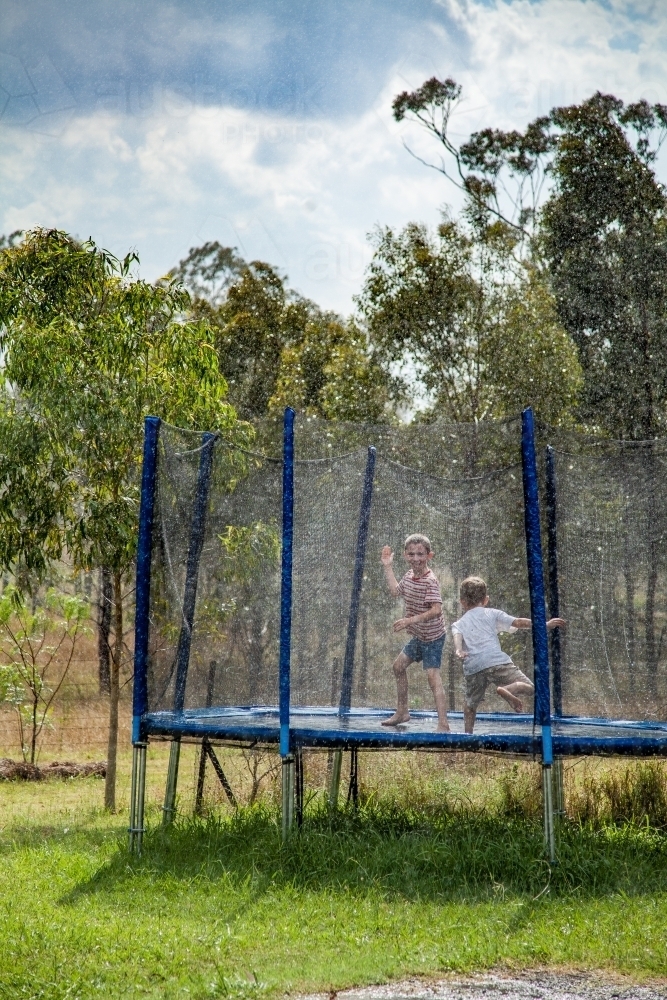 Two boys jumping on the trampoline in the rain - Australian Stock Image