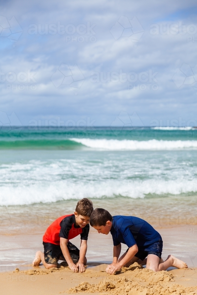 Two boys making sand castles and moats in the sand at the beach - Australian Stock Image