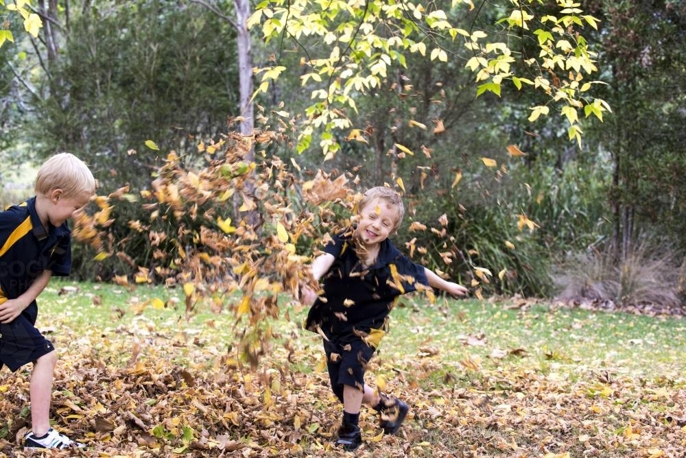 Two boys paying in autumn leaves wearing school uniform - Australian Stock Image
