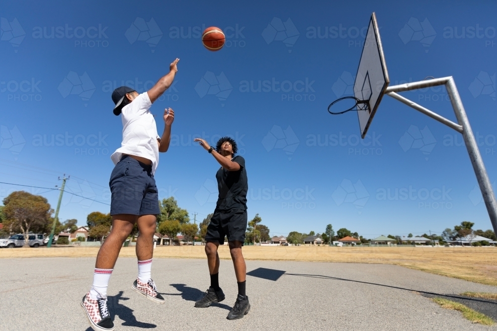 two boys shooting basketball one on one in country town - Australian Stock Image
