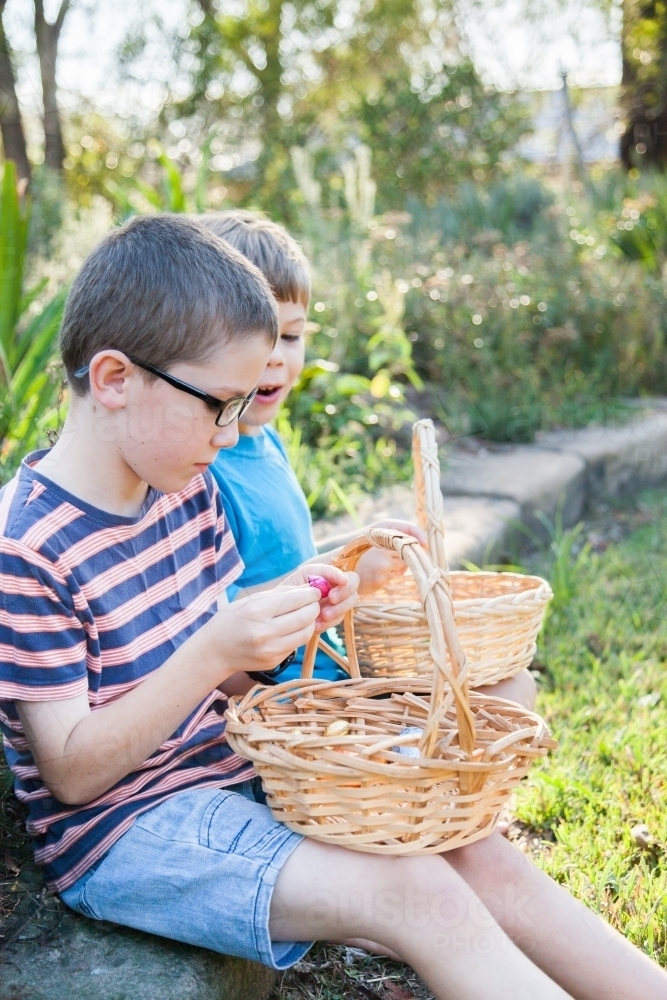 Two boys sitting eating chocolate eggs after Easter egg hunt - Australian Stock Image