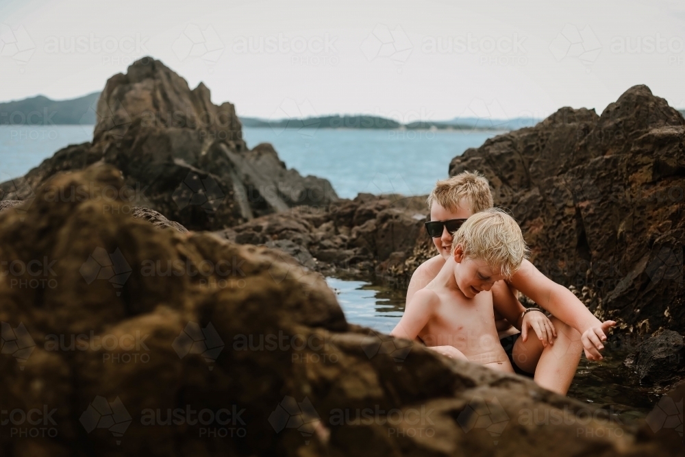 Two boys sitting in a rock pool at Coral Beach in the Whitsundays - Australian Stock Image