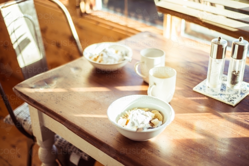 Two breakfast bowls and coffee mugs sitting on a sun drenched table - Australian Stock Image