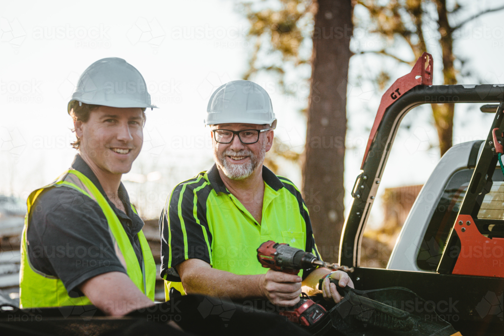 Two builders standing next to ute on construction site one man holding a drill - Australian Stock Image