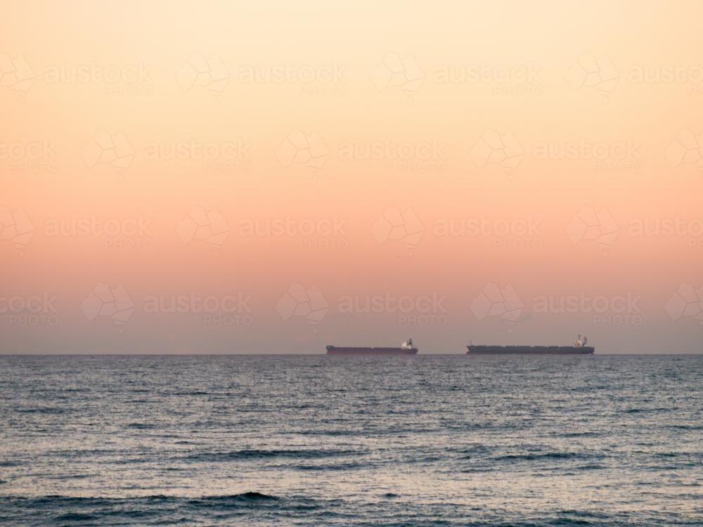 Two bulk carriers (ships) on the horizon at dusk - Australian Stock Image