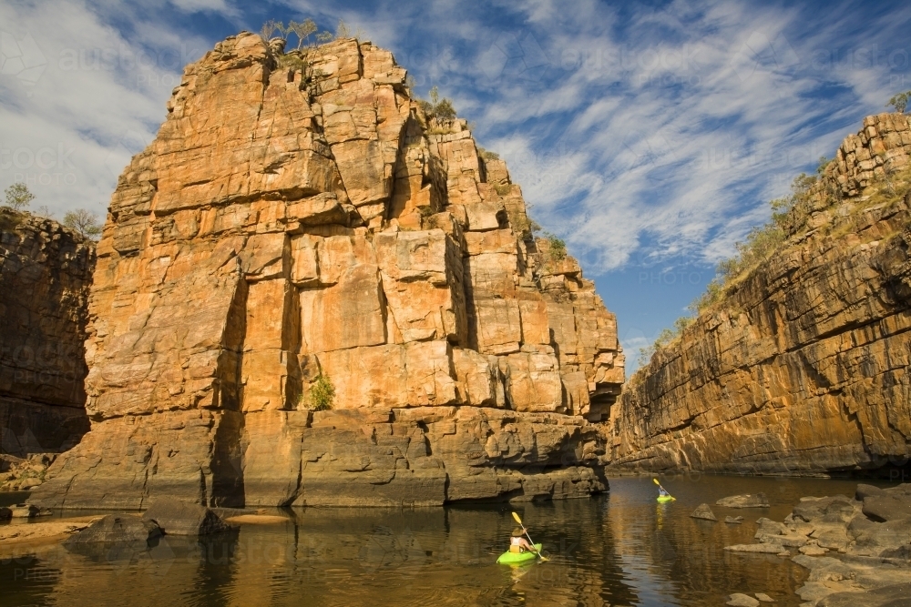 Two canoeists in a gorge with sandstone cliffs and cloud patterns in blue sky - Australian Stock Image