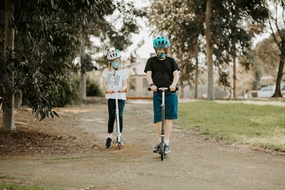 two caucasion children riding scooters wearing masks during the Corona COVID-19 pandemic - Australian Stock Image