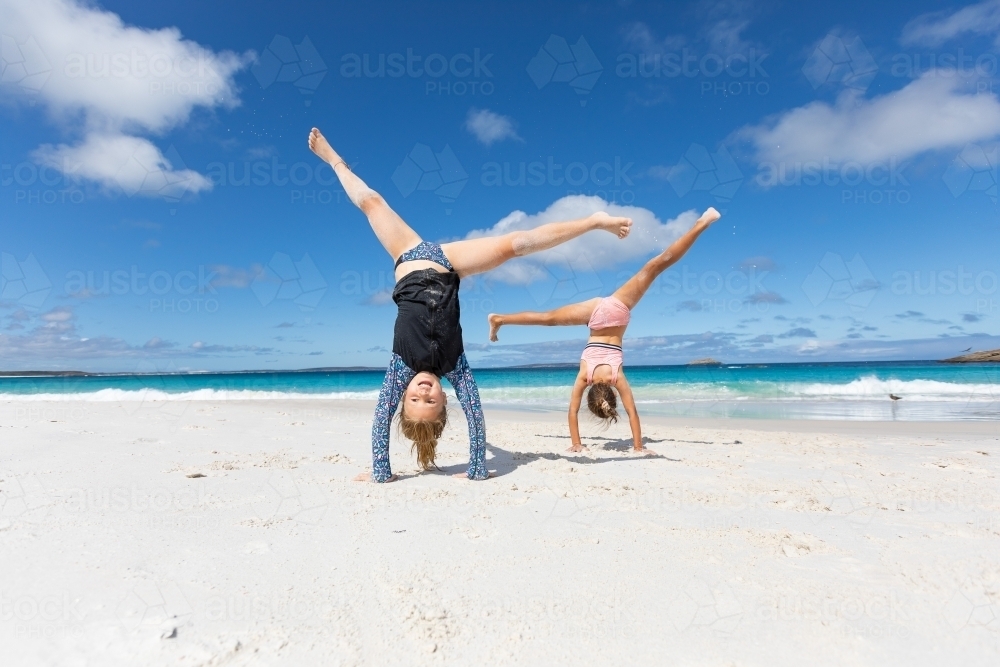 two children doing cartwheels on white beach sand - Australian Stock Image