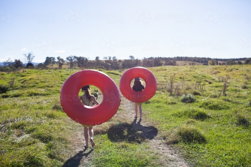 Two children walking on a track carrying inflatable rings - Australian Stock Image