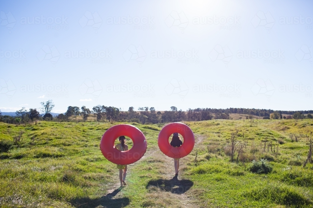 Two children walking on a track carrying inflatable rings - Australian Stock Image