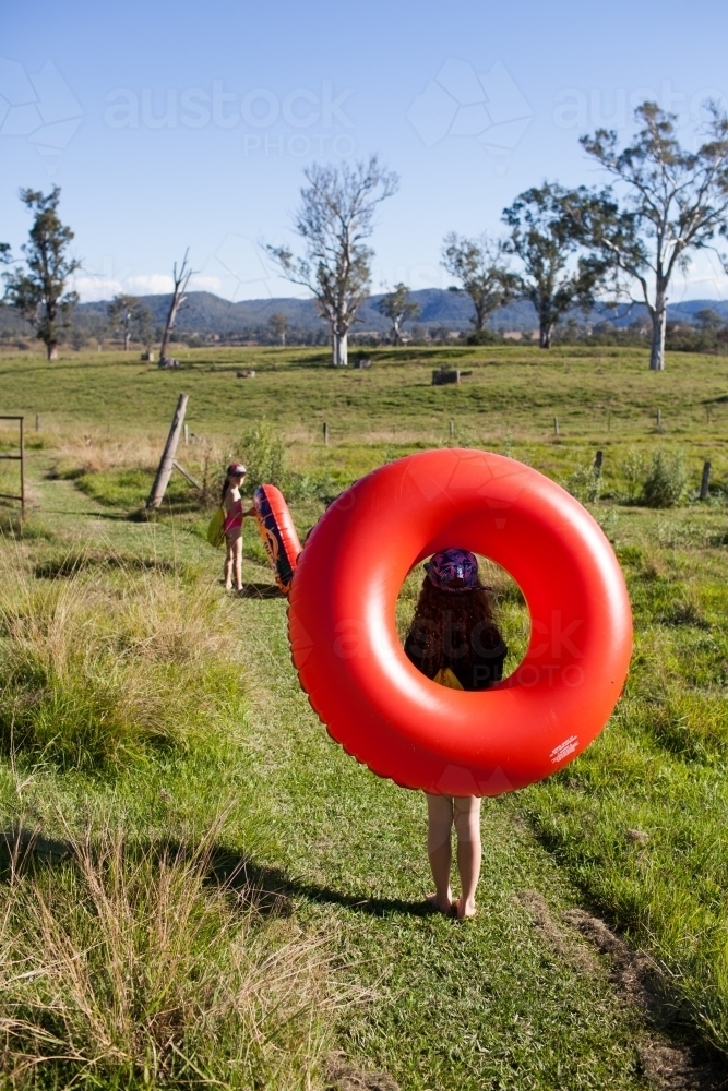 Two children walking on a track carrying inflatable rings - Australian Stock Image
