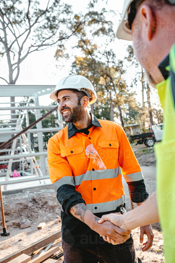 Two construction workers shaking hands on worksite - Australian Stock Image