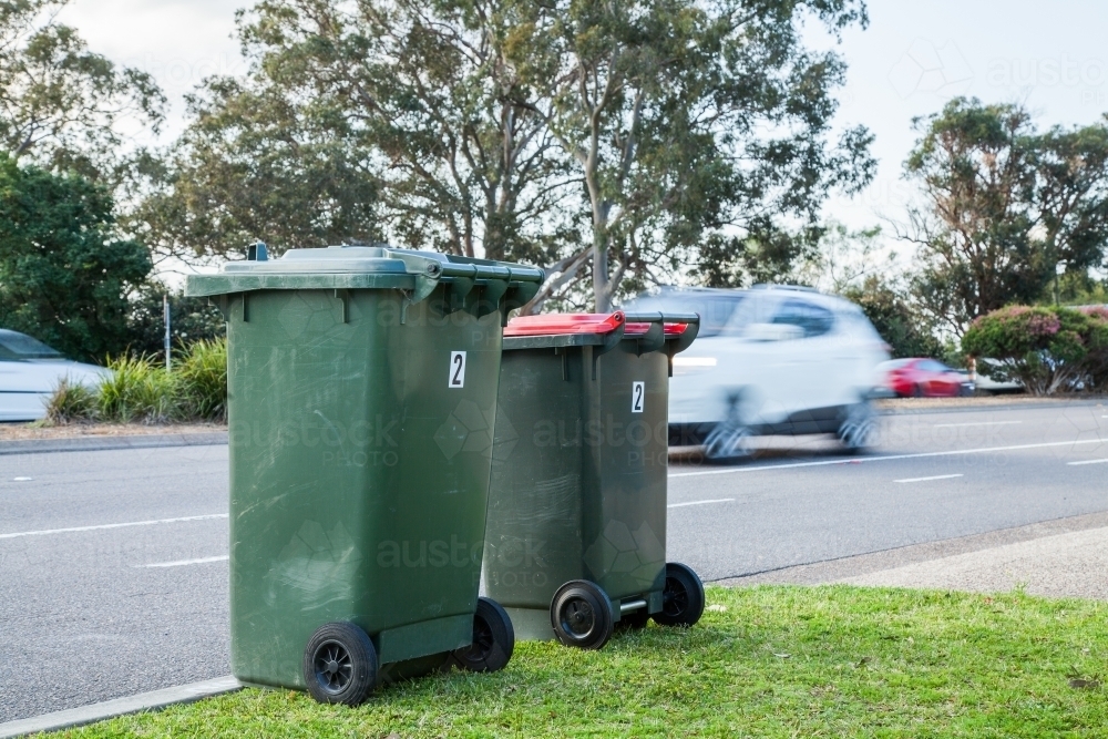 Two council bins awaiting collection beside a busy road - Australian Stock Image