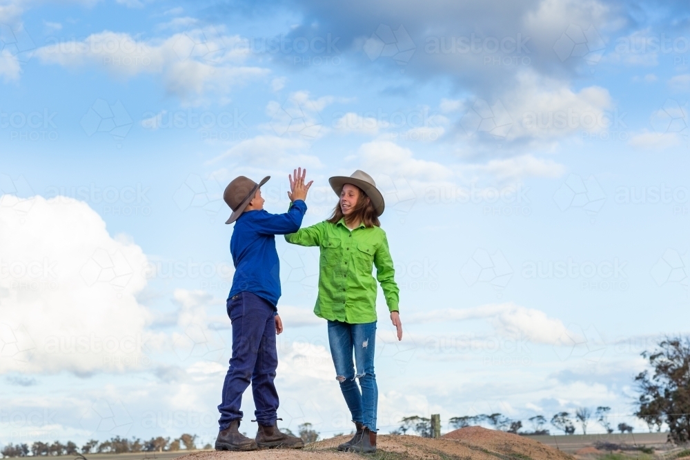 Two country kids high-fiving outdoors against a cloudy sky - Australian Stock Image