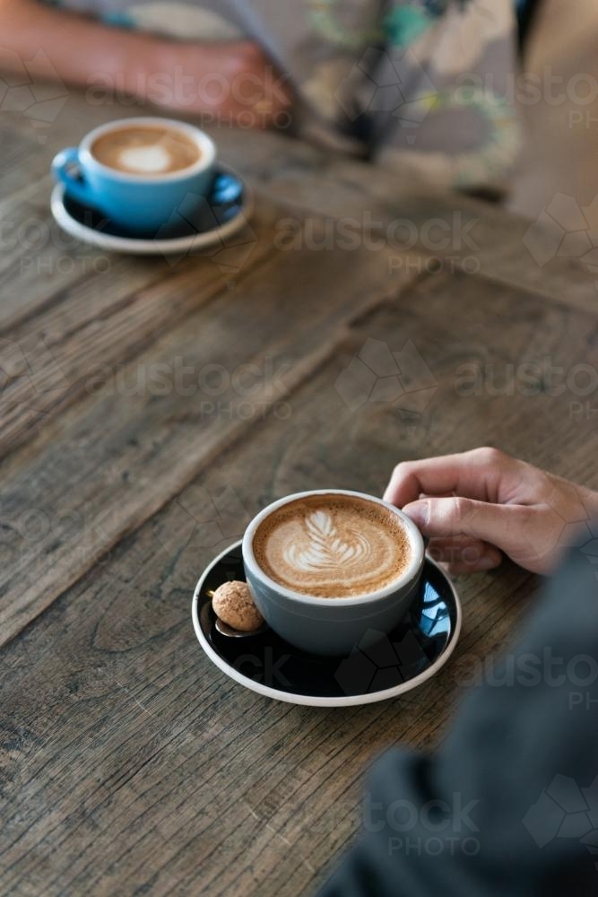 Two cups of coffee on a wooden table with people - Australian Stock Image