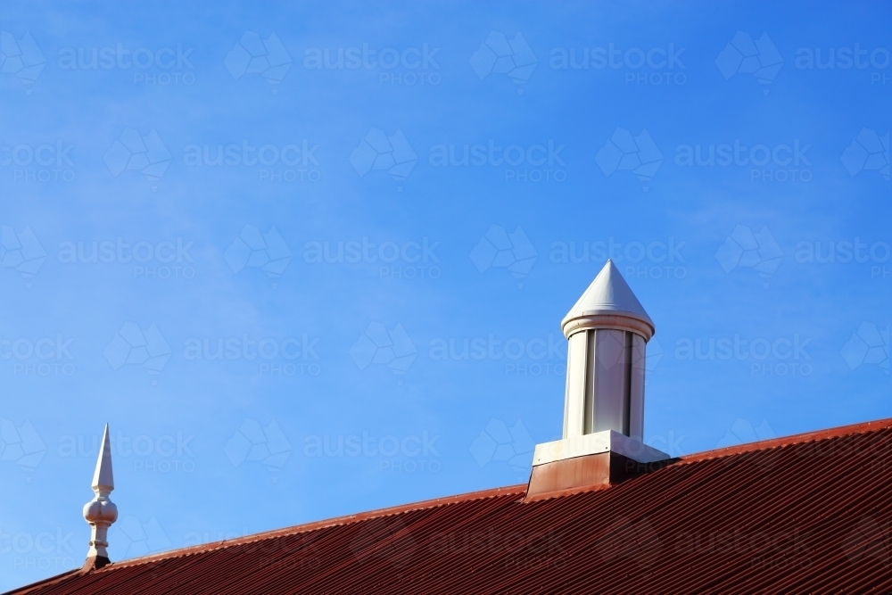 Two different roof spire type ornaments atop a red roof and a bright blue sky - Australian Stock Image