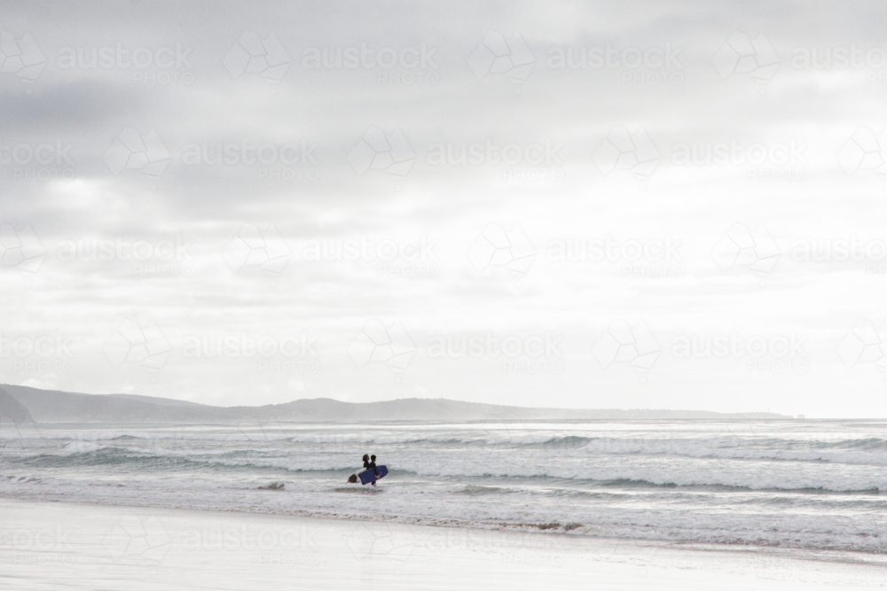 Two distant surfers entering the water - Australian Stock Image