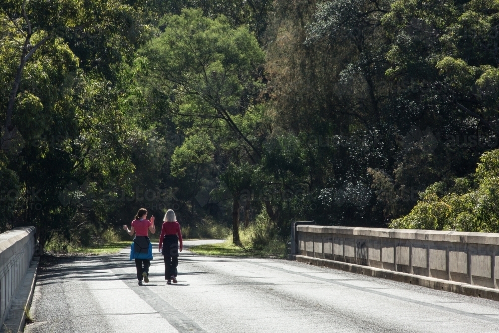 Two distant women walking along a closed roadway towards bushland - Australian Stock Image
