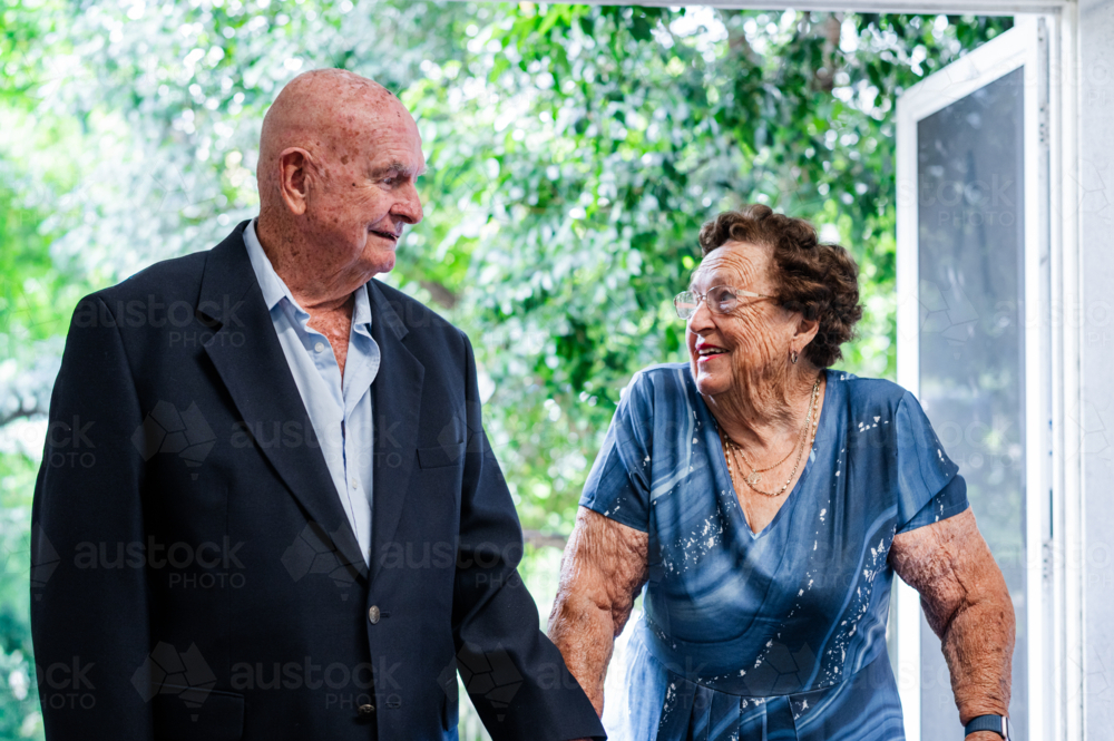 Two elderly individuals engage in conversation while walking through an open door - Australian Stock Image