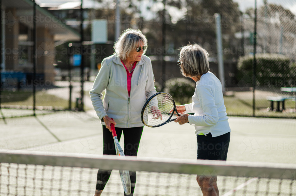 Two elderly women enjoying a friendly game of tennis at a sunny local court - Australian Stock Image