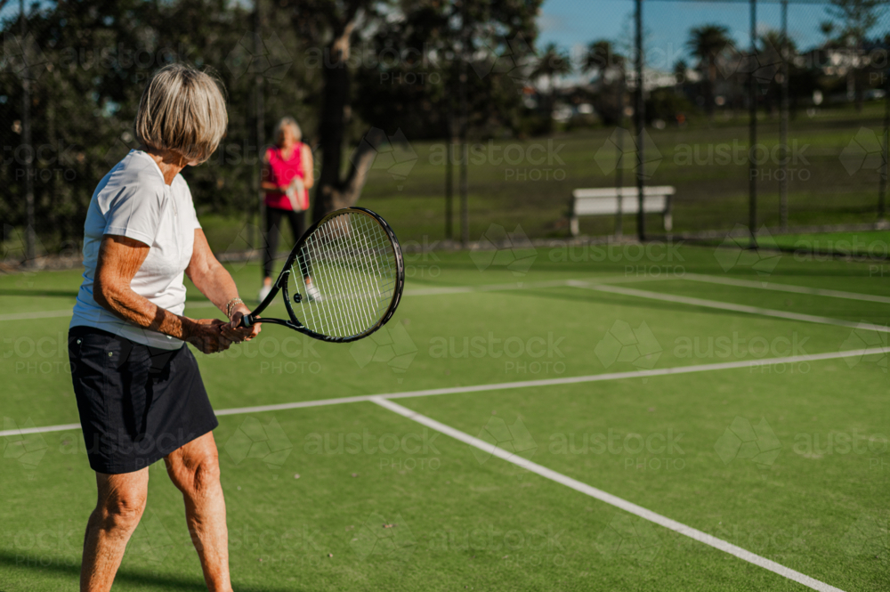 Two elderly women enjoying a game of tennis outdoors, showcasing active lifestyle and friendship. - Australian Stock Image