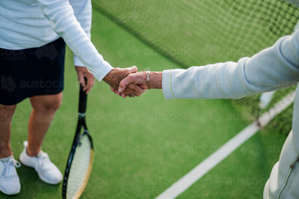 Two elderly women shaking hands, celebrating sportsmanship after their tennis game. - Australian Stock Image