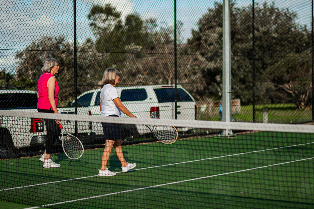 Two elderly women with tennis racquets walking on a tennis court - Australian Stock Image
