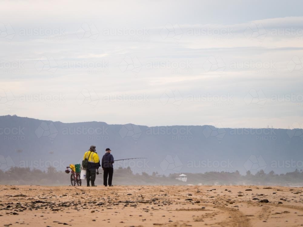 Two fishermen talking on the beach in the distance - Australian Stock Image