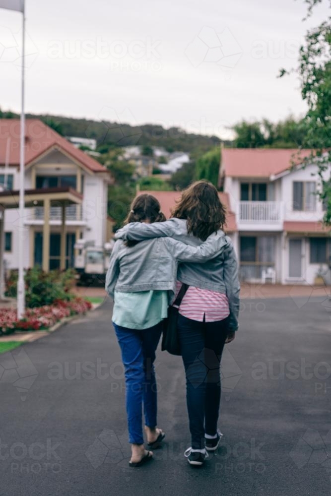 two friends or sisters walking together, hugging - Australian Stock Image