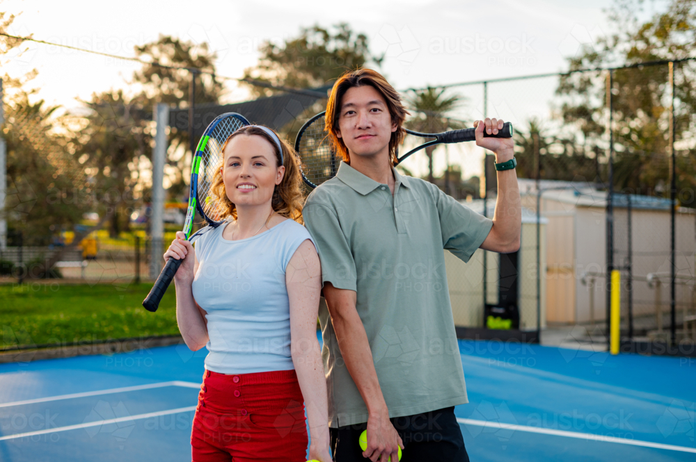 Two friends stand on a tennis court, holding racquets, ready for a fun game in the sun - Australian Stock Image
