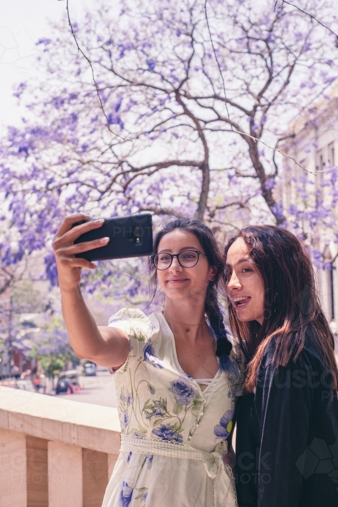 two friends taking a selfie in front of jacarandas in bloom - Australian Stock Image