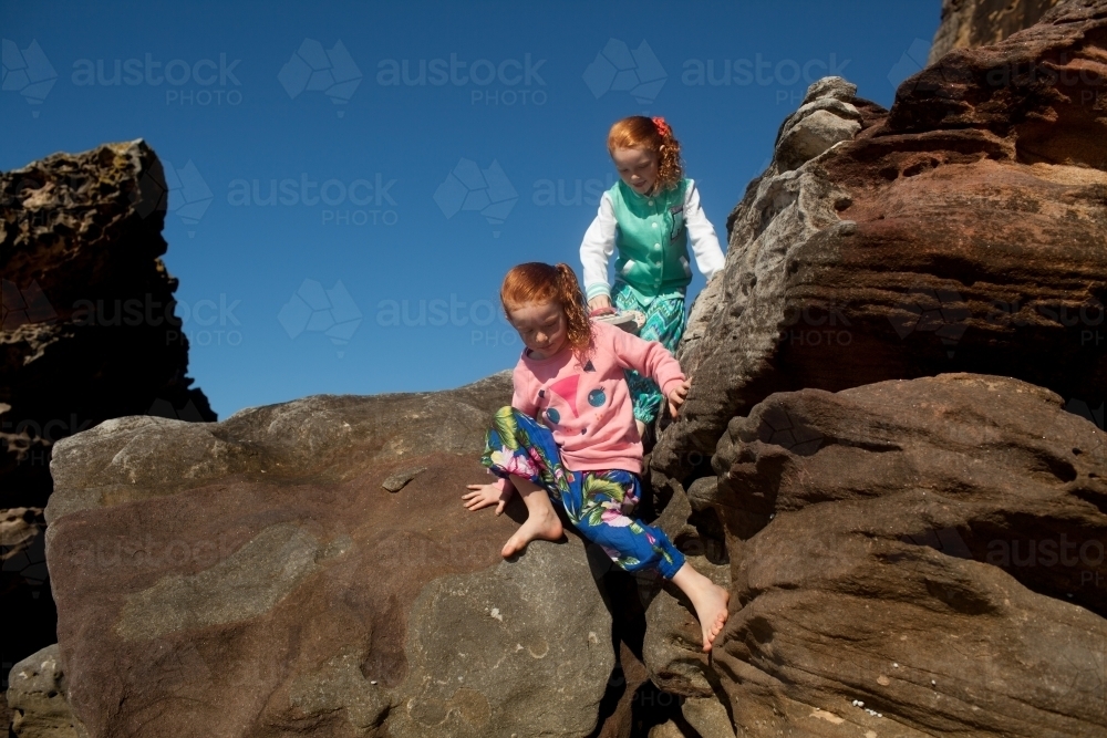 Two girls climbing over rocks - Australian Stock Image