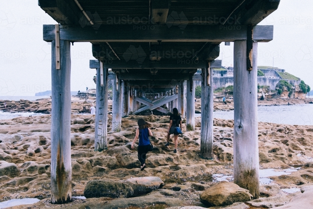 Two girls exploring under a bridge over rocks and water - Australian Stock Image