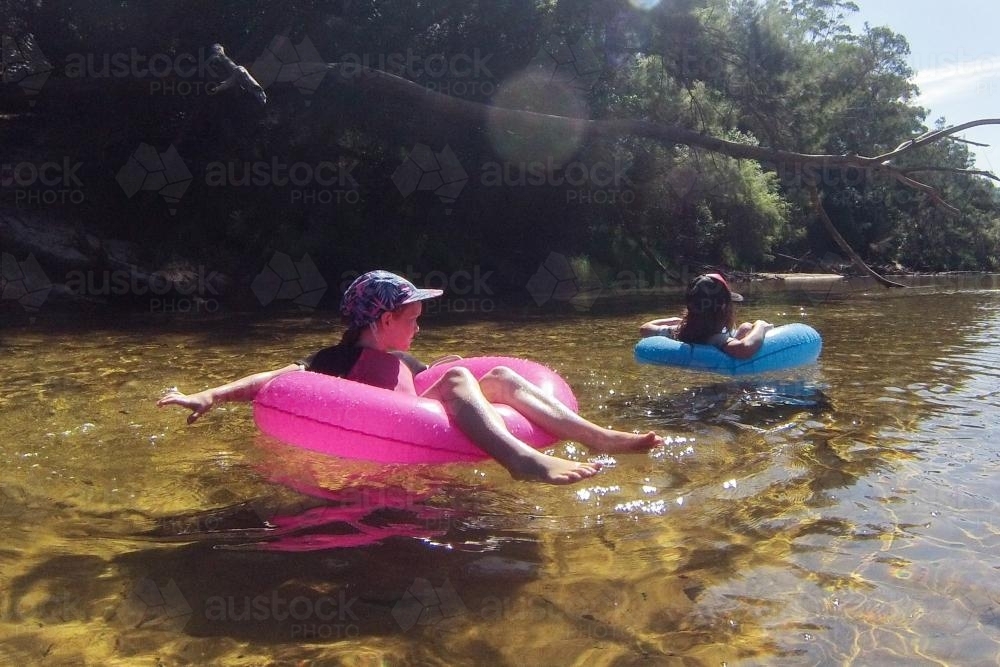 Two girls floating on a river in inflatable rings - Australian Stock Image