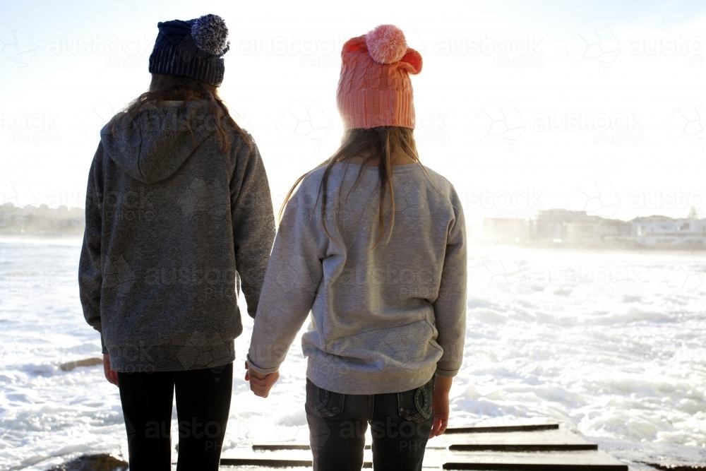 Two girls holding hands on a boat ramp in the afternoon light - Australian Stock Image