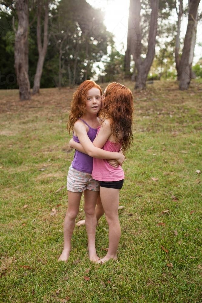 Two girls hugging and telling secrets in a field - Australian Stock Image