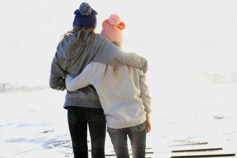 Two girls hugging each other looking out at the ocean - Australian Stock Image