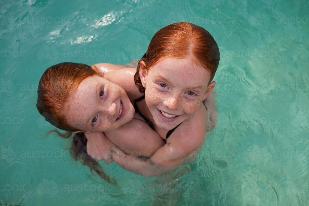 Two girls hugging in a backyard swimming pool - Australian Stock Image