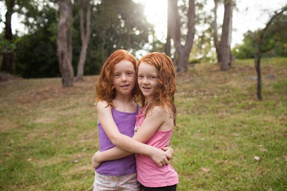 Two girls hugging in a grassy field - Australian Stock Image