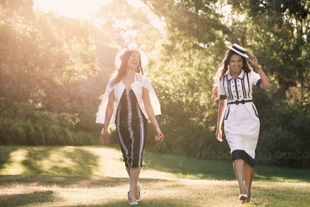 Two girls in dresses walking in the park backlit by sun - Australian Stock Image