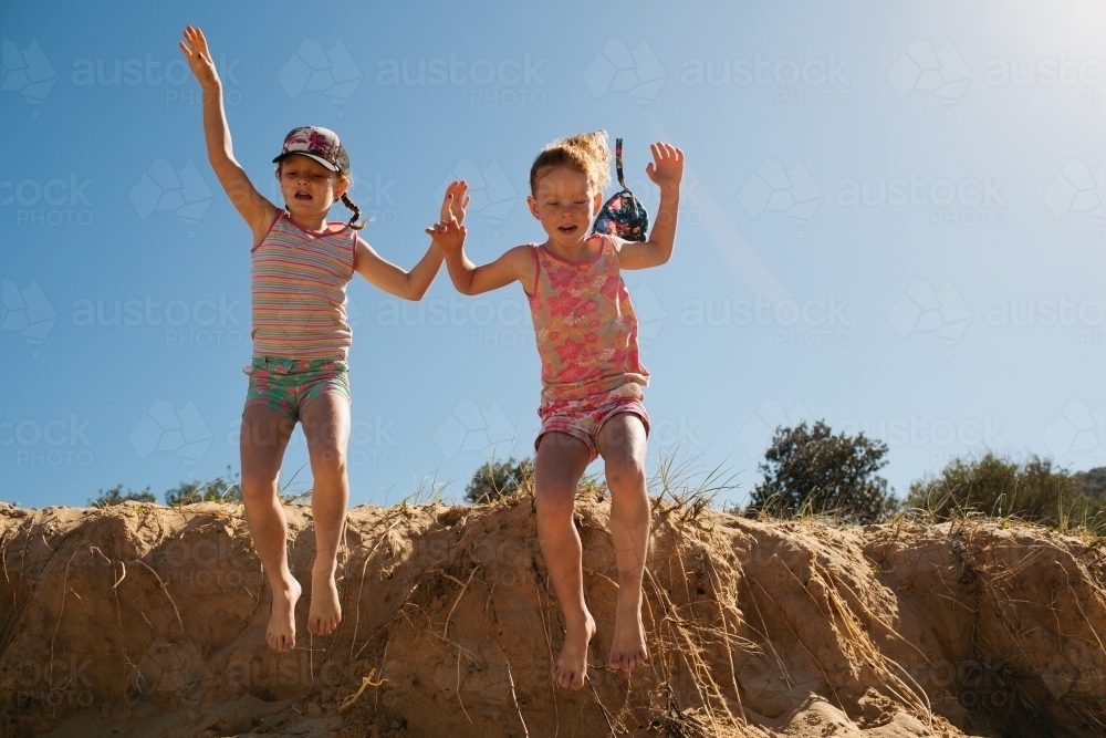 Two girls jumping off a sand dune at the beach - Australian Stock Image