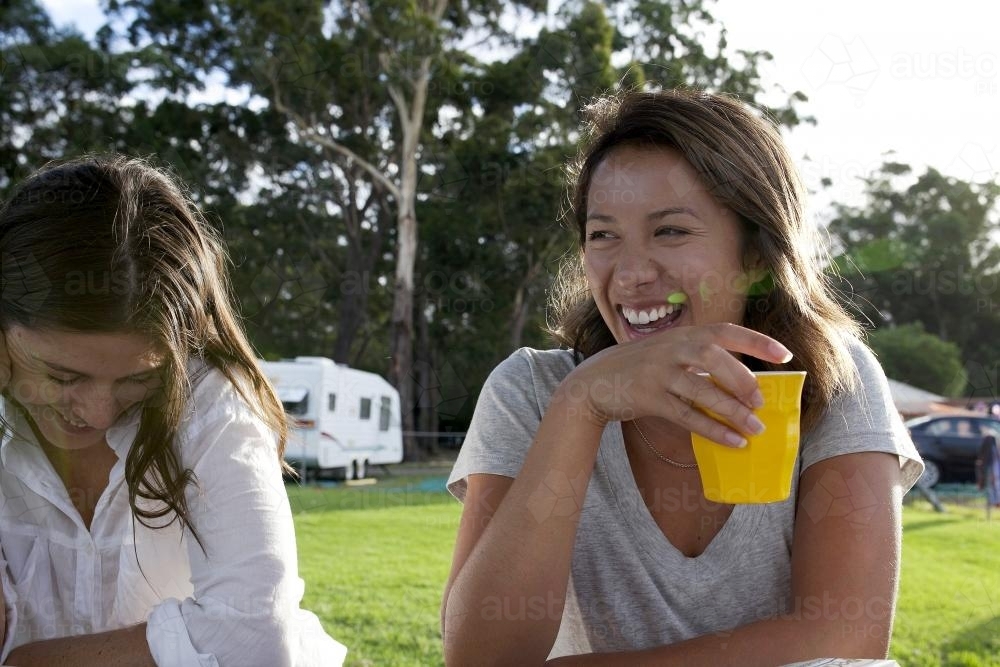 Two girls laughing sitting at a picnic table - Australian Stock Image
