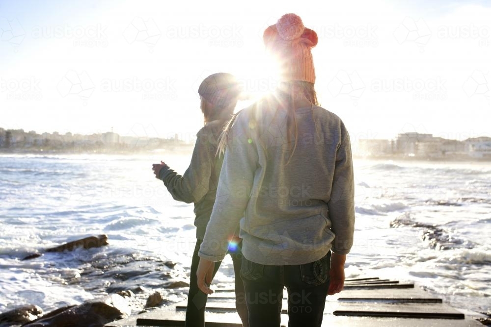 Two girls on a boat ramp by the ocean in the afternoon light - Australian Stock Image