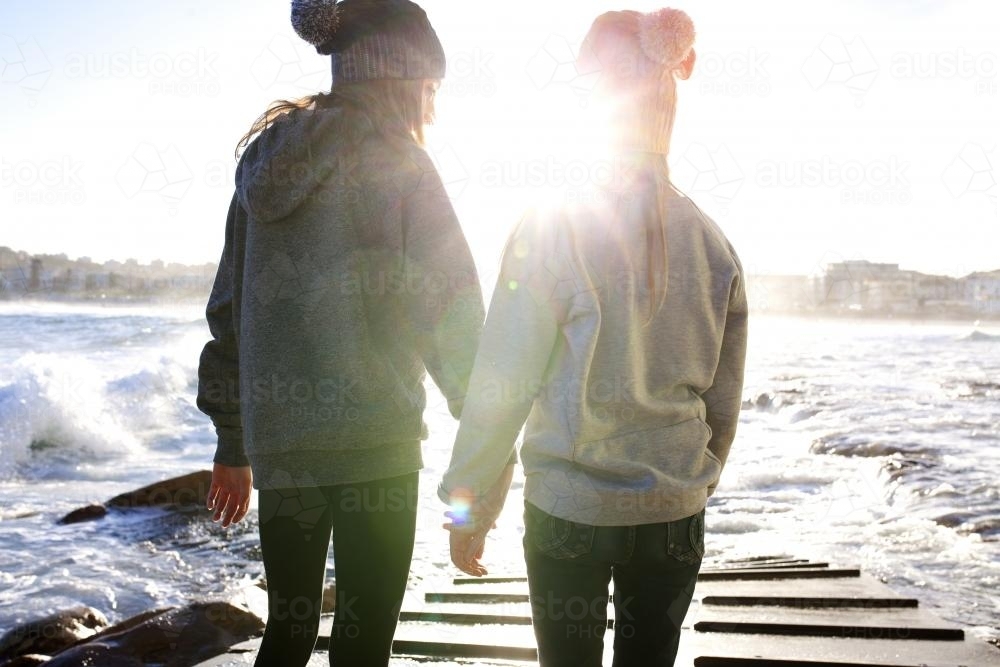 Two girls on a boat ramp by the ocean in the afternoon light - Australian Stock Image