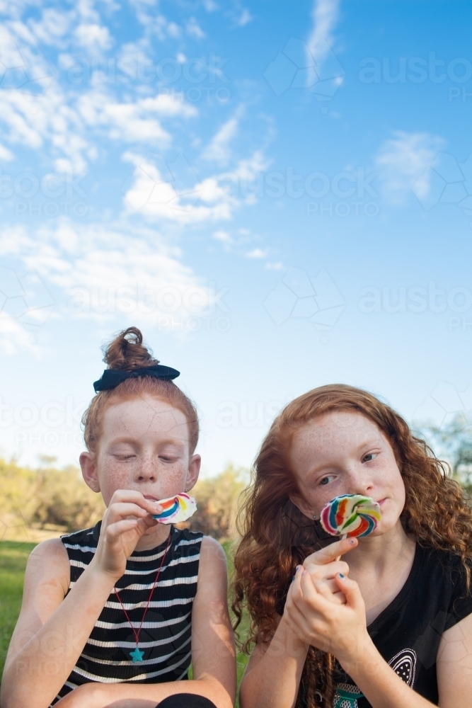 Two girls outside eating rainbow lollipops - Australian Stock Image