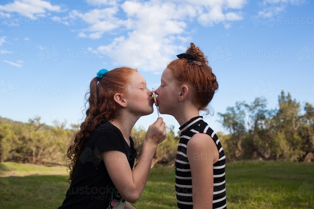 Two girls outside kissing a rainbow lollipop - Australian Stock Image