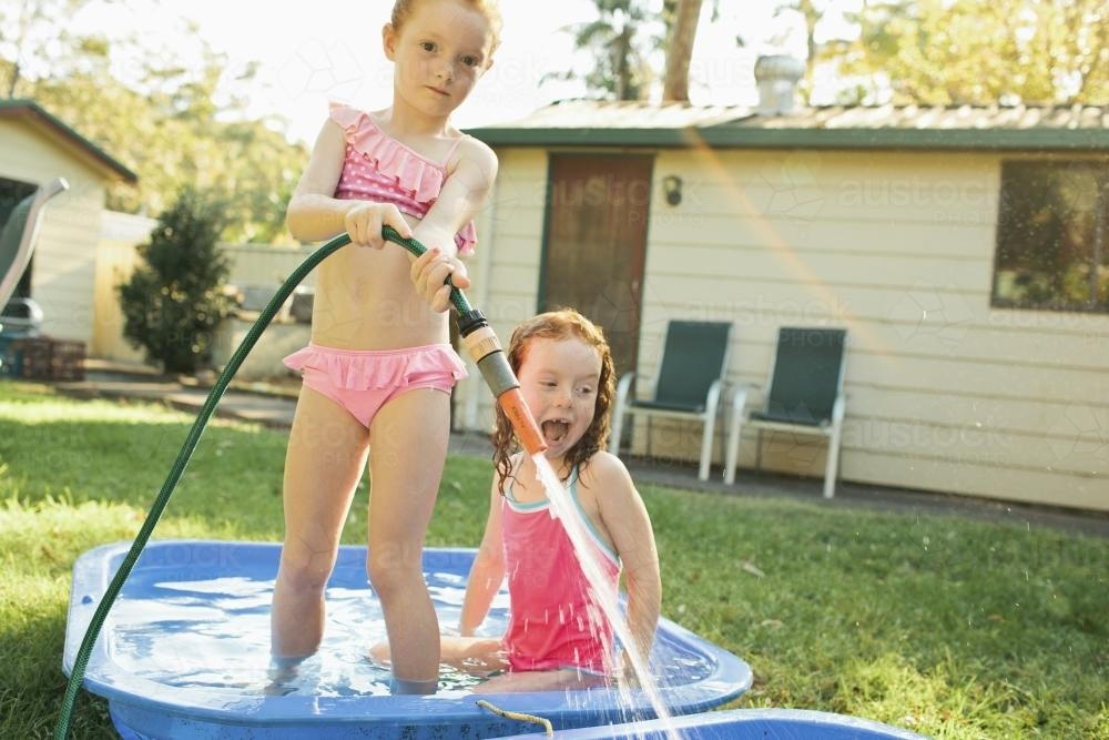 Two girls playing in a backyard paddling pool - Australian Stock Image