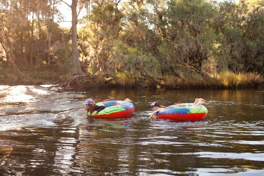 Two girls playing on inflatable rings on a river - Australian Stock Image